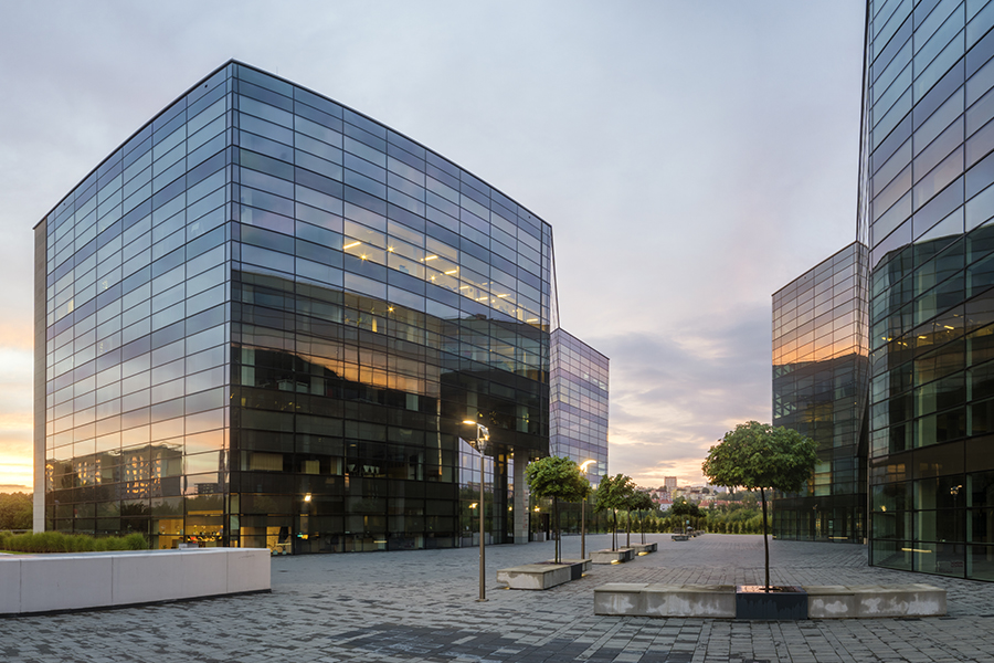Business Insurance - Modern Office Building in the Evening with Landscaped Trees and City in the Background